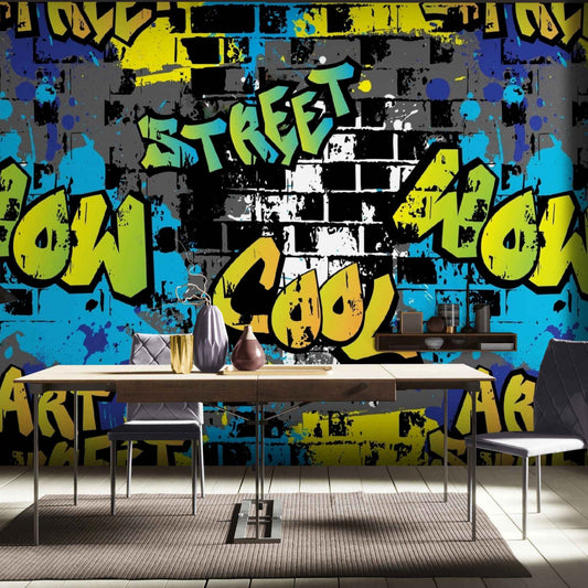 An image of a wallpaper with a graffiti design, featuring bold and abstract shapes, lines, and lettering in various shades of black, white, and gray. The wallpaper is peel and stick, making it easy to install and remove without causing damage or leaving residue on the wall surface. It is ideal for creating an urban chic look in modern interiors, such as living rooms, bedrooms, or home offices, where it adds a touch of edgy and artistic vibe to the decor.