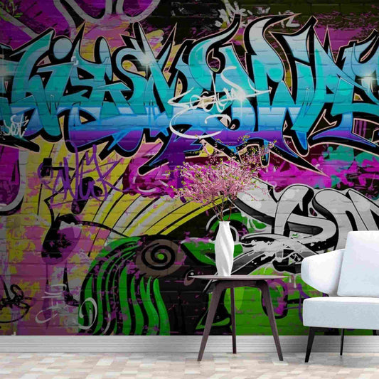 Photo of a wall covered in a graffiti wallpaper mural that can be easily installed using the peel and stick method. The mural features vibrant and colorful graffiti art with various styles and designs, including bold text, abstract shapes, and patterns commonly seen in urban street art. The peel and stick feature of the wallpaper makes it a convenient and hassle-free option for decorating walls with an edgy and trendy aesthetic.